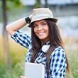 A young woman wearing plaid and a hat smiling and holding her hat.