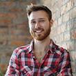 A young man in plaid smiling. It's a bright sunny day.