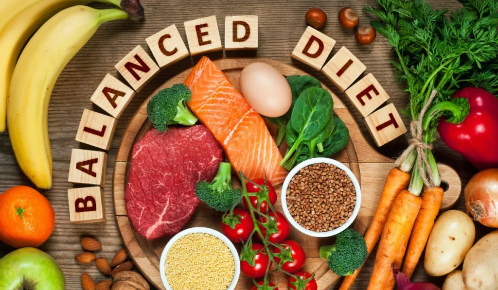 A wide array of foods including meats, eggs, vegetables, and fruit underneath wooden block letters that say "balanced diet".