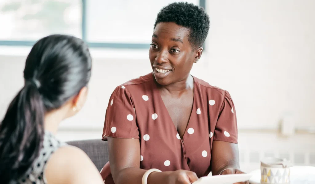 A Black woman and dark-haired woman conversing.