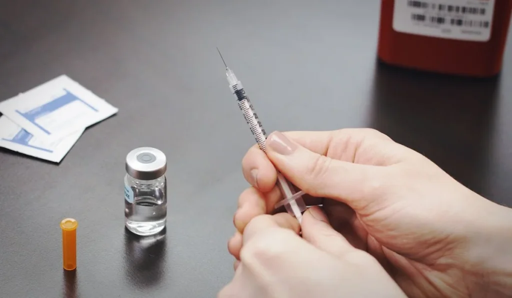 A woman holding a medical syringe next to her bottle of HRT.