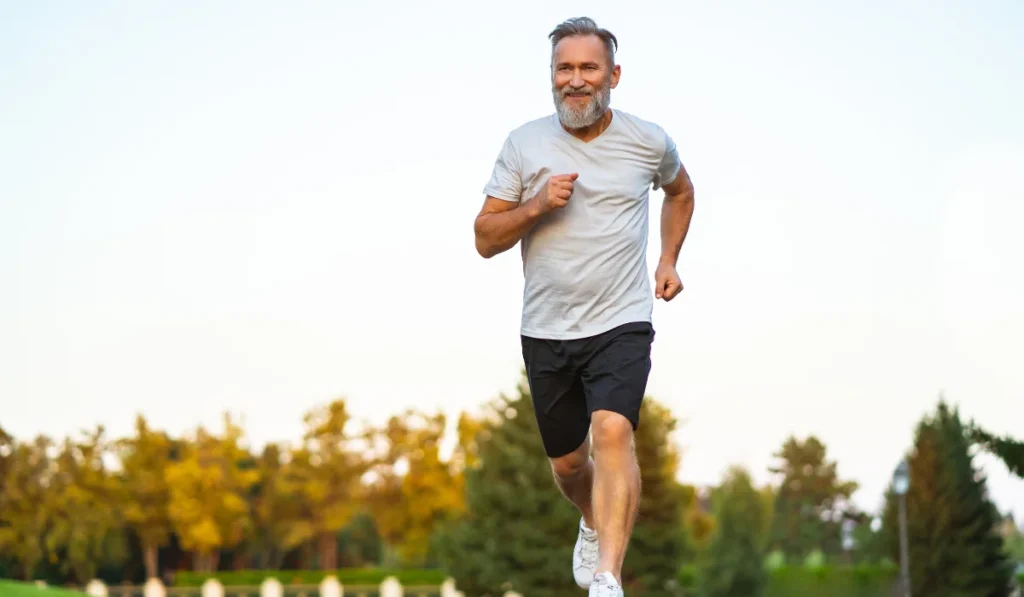 An older man with gray hair and beard running for exercise on a bright sunny afternoon.