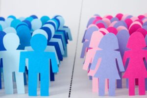 Paper cutouts of men and women in blue and pink, respectively, standing up on a white background with a black dotted line drawn between them.