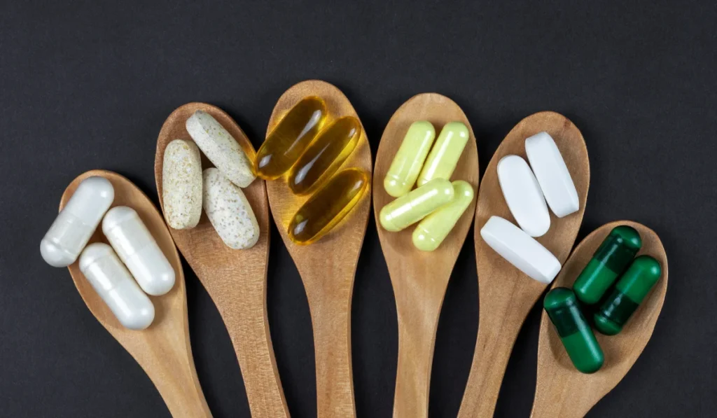 6 wooden spoons with piles of different colored pills and capsules on each.