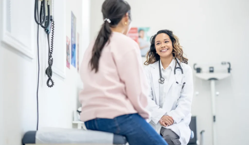 A doctor and patient sitting in the examination room. The patient is speaking to the doctor who is smiling.